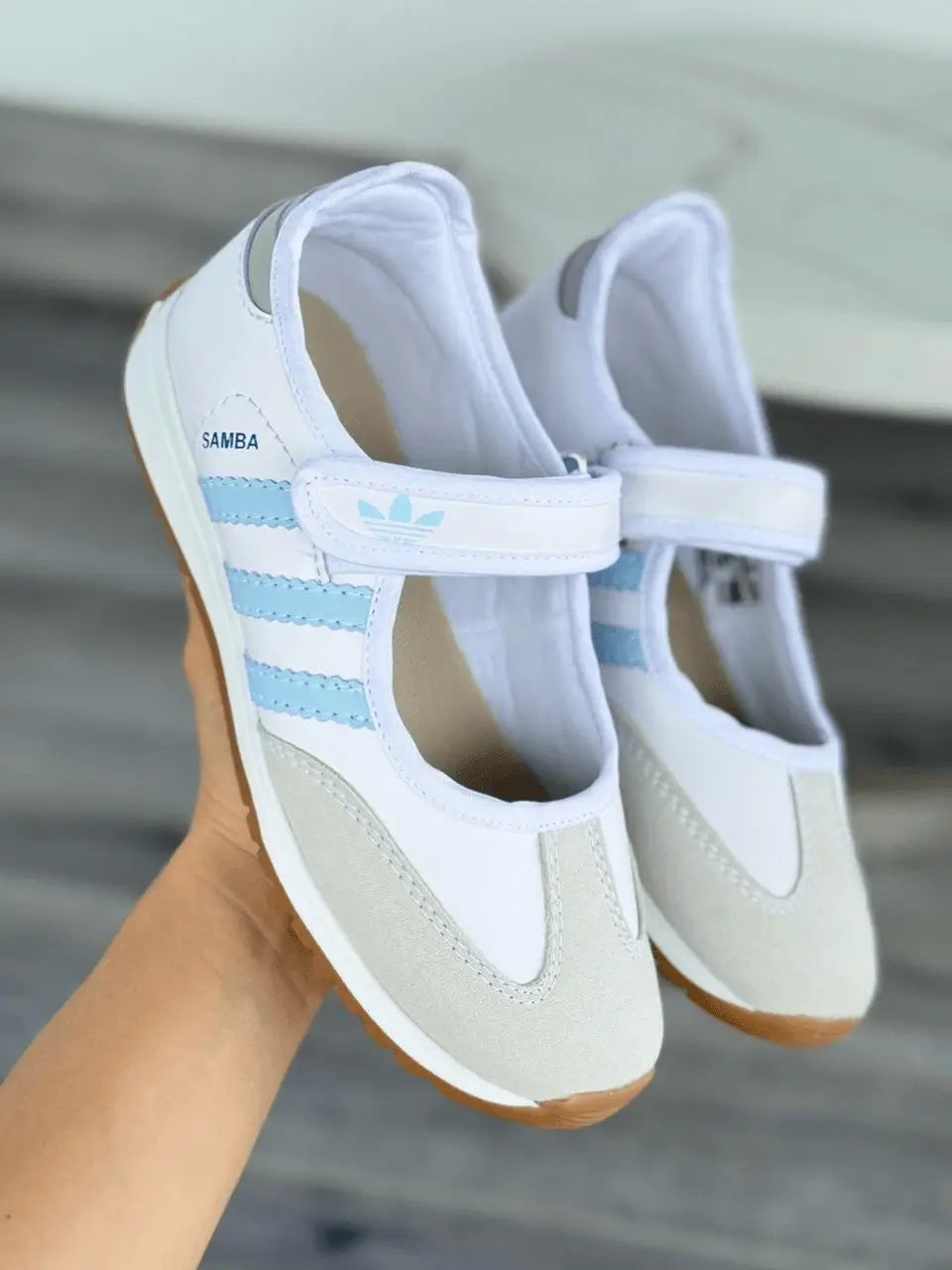 Par de baletas deportivas en tono blanco con franjas celestes, correa de velcro ajustable, suela antideslizante de goma y refuerzo en puntera, calzado ligero, transpirable y cómodo para uso diario y estilo casual.