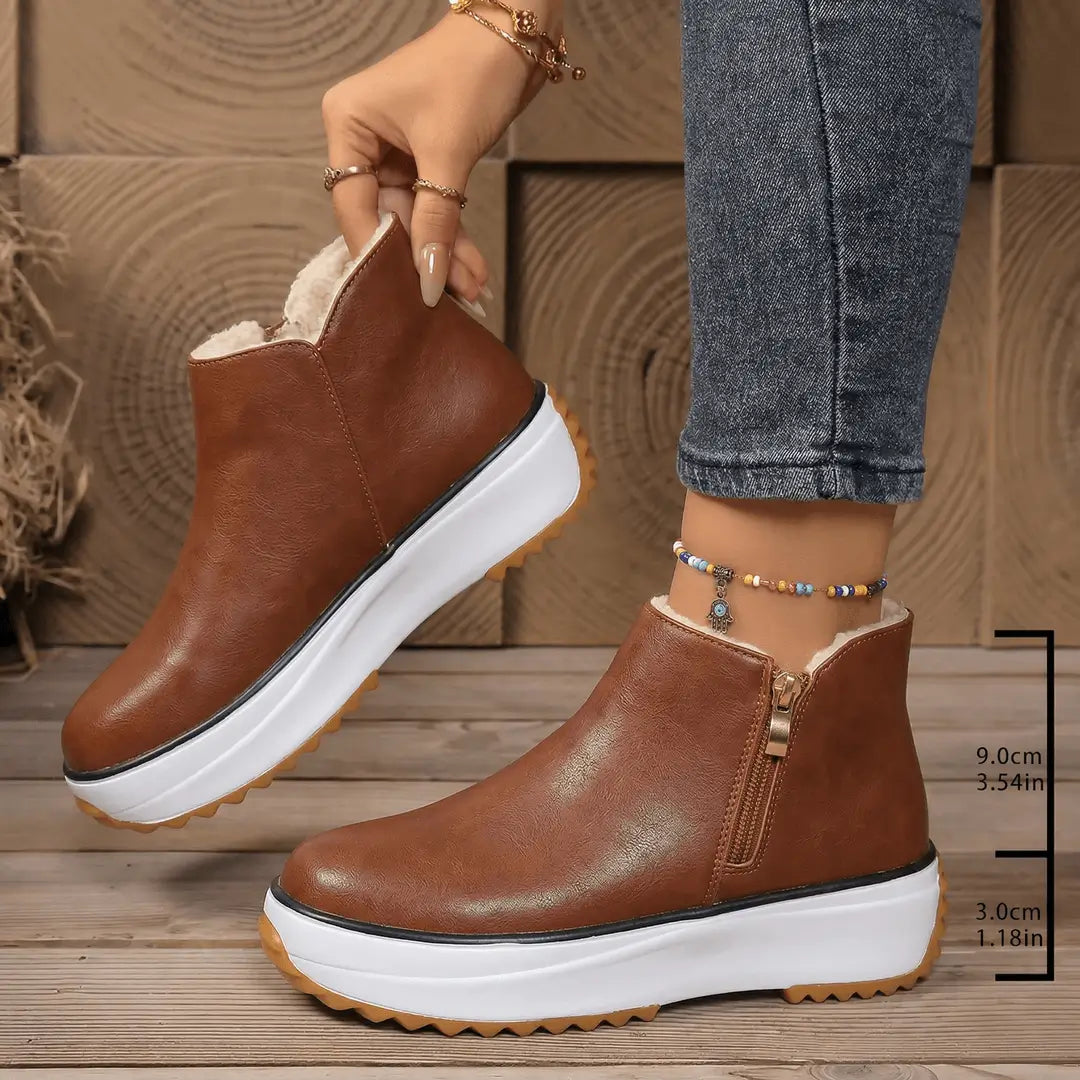 Botín de mujer color café con exterior en cuero sintético y forro de peluche, suela plataforma blanca antideslizante de 3 cm y tacón de 9 cm, cierre lateral para un ajuste seguro y estilo urbano, ideal para frío y uso diario cómodo.