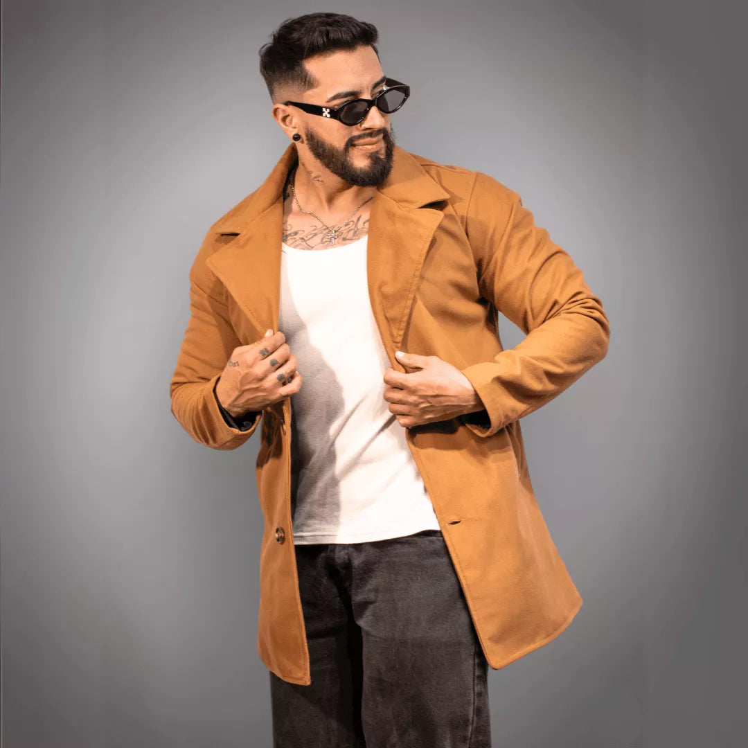 Gabardina color camello para hombre de estilo moderno y casual. El modelo posa con gafas de sol, camisilla blanca y jeans grises oscuros. Ideal para un outfit de moda en ciudades colombianas como Bogotá o Medellín. Calidad garantizada
