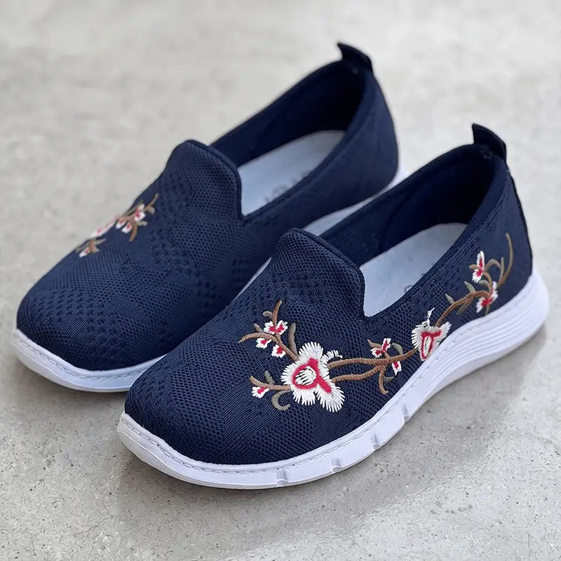 Zapatillas Florenza azul marino con bordado floral en blanco y rosa, suela blanca ligera antideslizante, tejido transpirable y plantilla acolchada para caminar todo el día con comodidad y estilo casual