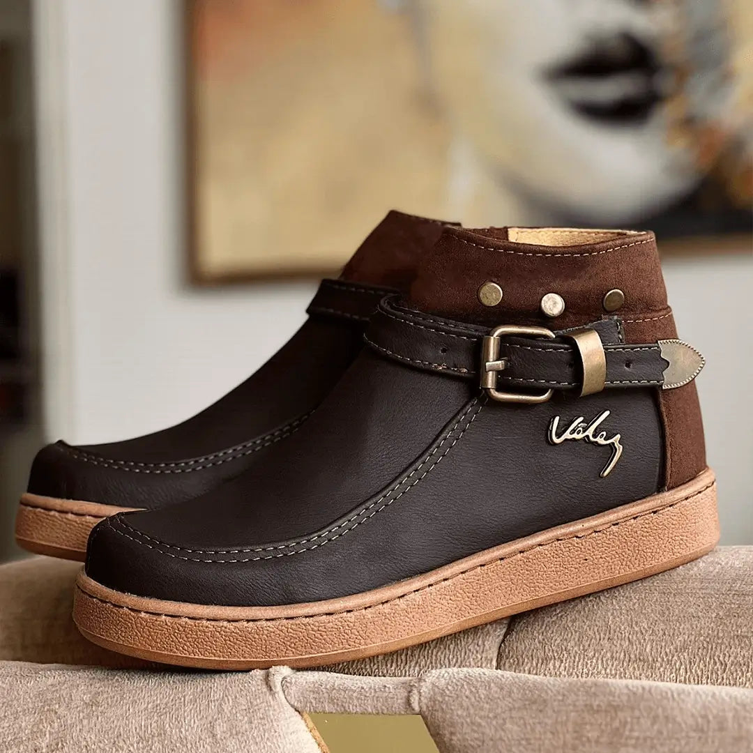 Botín femenino en cuero sintético y gamuza color café oscuro, diseño elegante con hebilla ajustable, suela antideslizante y cómoda ideal para uso diario y clima frío, calzado duradero y moderno para complementar tu look casual y profesional.